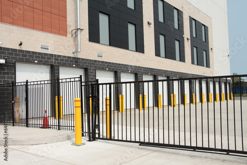 line row of exterior outdoors outside building public storage white garage units behind black metal fence mechanical gate on cement pavement