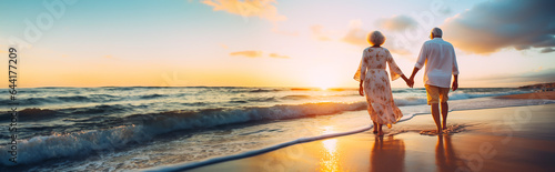 Senior couple walking along a beach in the sunset. Concept of retirement, mature love and travel. Shallow field of view with copy space.