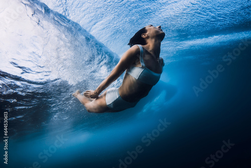 Surfgirl dive underwater under wave. Duck dive under barrel wave in blue ocean