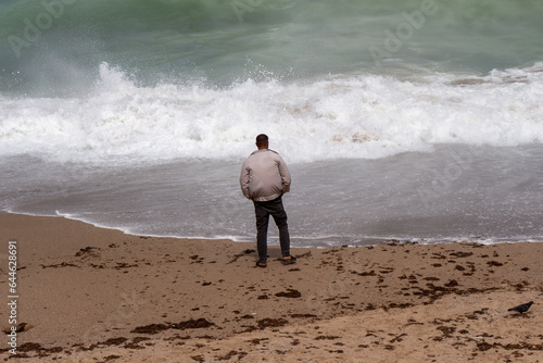 Algerian man from behind looking standing on a beach and looking at a big wave, Algiers, Alger, Algeria.