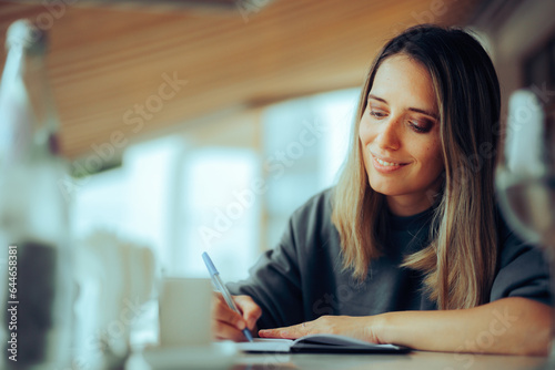 Happy Woman Writing a Food Journal in a Restaurant. Busy freelance worker keeping a diary and an idea list anywhere she goes 