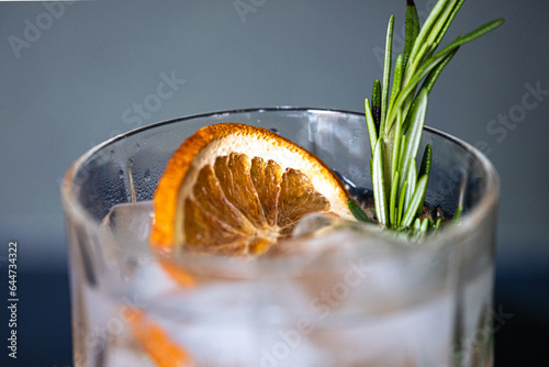 Glass of gin and tonic cocktails with ice, sprig of rosemary and sliced dry orange on a blue background. Copy space