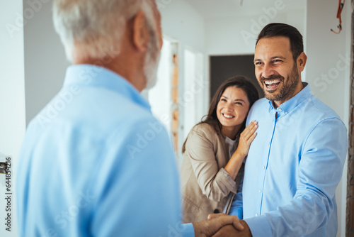 Friendly Real Estate Agent and young couple shaking hands standing in hallway, real estate agent handshaking clients at meeting, showing selling buying property for rent sale
