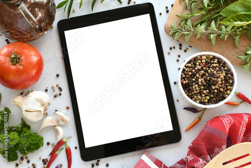 Tablet computer with mock up white screen in kitchen with food flat lay background. Online grocery shopping, takeout, food delivery app ads or recipe concept.