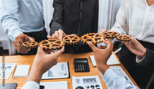 Office worker holding cog wheel as unity and system teamwork in corporate workplace with piles of business paper and financial report on meeting table. Business people with business success. Concord