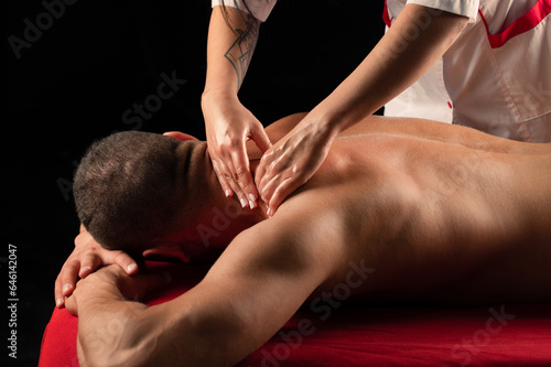Man having massage in massage salon. Sports massage. Therapist massaging shoulders of a male athlete, working with trapezius muscle. Man enjoying massage at spa.