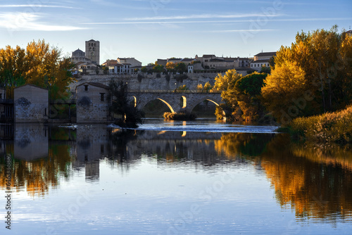 View of the city of Zamora and watermills and the romanesque cathedral in autmn at sunset reflected in the Duero river. Spain