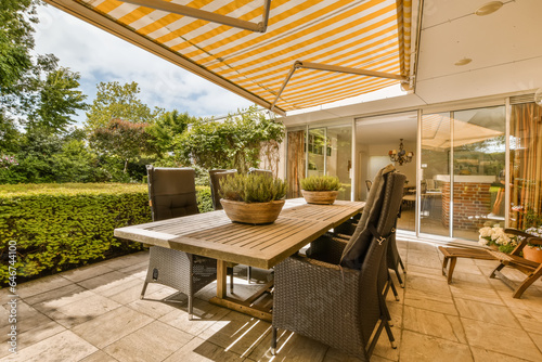 an outdoor dining area with table and chairs under the awning on a sunny day in the patio is surrounded by lush green trees