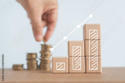 increasing graph bar on wooden cube block with blurred hand putting coins to stacking for money saving profit and business investment growth concept