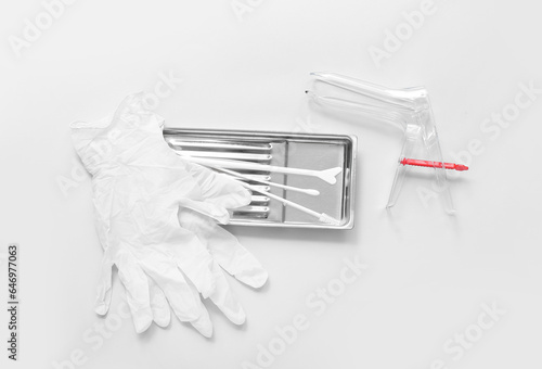 Medical gloves with gynecological speculum and pap smear test tools on light background