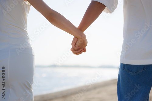 手を握ってビーチを歩いている若いアジア人のカップル