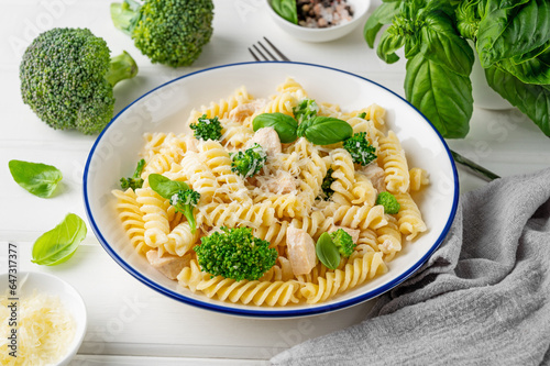 Delicious broccoli and chicken fusilli pasta with parmesan cheese and fresh basil in a bowl on a white wooden background. Healthy comfort food.