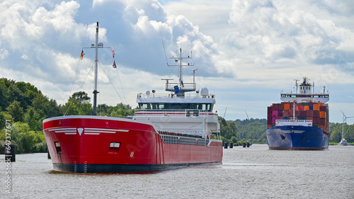 Dwa statki floty handlowej - kontenerowiec i drobnicowiec płyną przez kanał Kiloński w Niemczech w słoneczny dzień.