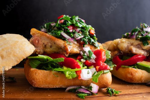 Chimichurri Chicken Sandwich on a Wooden Cutting Board: Open-faced sandwich topped with avocado, roasted peppers and arugula