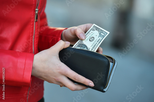 young woman hand take out one dollar bills from her wallet on street