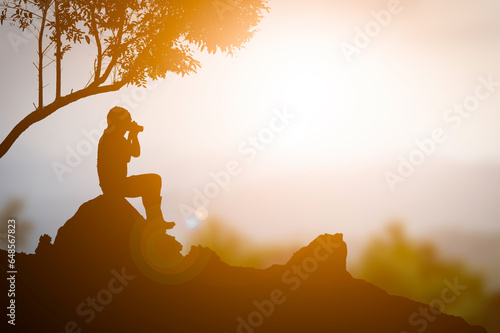 A tourist man sitting on the rock and take photo sunset orange color background
