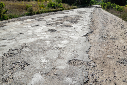 Bad road, cracked asphalt with potholes and big holes. Potholes on the road with stones on the asphalt. The asphalt surface is destroyed on the road. Bad condition of the road, needs repair.