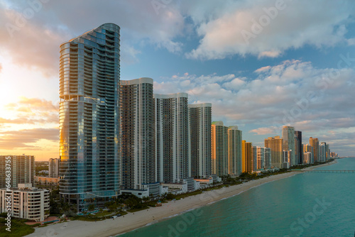 Aerial view of Sunny Isles Beach city with luxurious highrise hotels and condos on Atlantic ocean shore at sunset. American tourism infrastructure in southern Florida