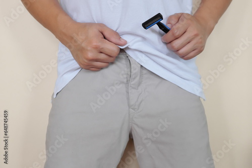 Closeup of male crotch with hand holding a shaver. Shave pubic hair down under concept. Men's Fitness, grooming and health. 