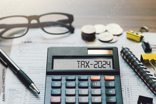 Word Tax 2024 on the calculator. Business and tax concept.Calculator, coins, book, tax form, and pen on table.Tax deduction planning.Financial research, government taxes, and calculation tax return