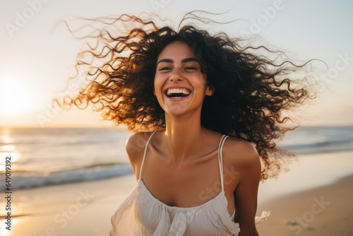 Woman with curly hair is captured smiling on beach. This picture can be used to depict happiness, relaxation, vacations, or summer vibes.