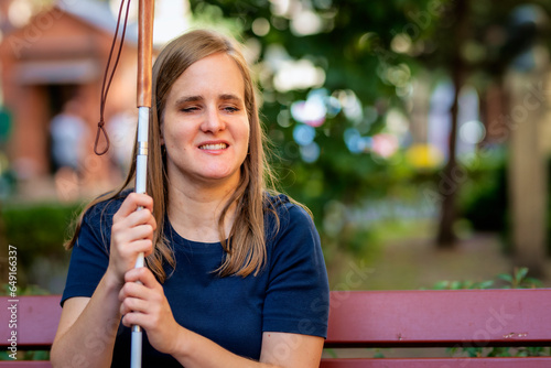 A visually impaired woman holding a white cane and sitting on a bench in the city