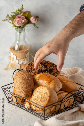 mano de hombre cogiendo panes en una canasta sobre un fondo blanco servidos en la mesa. con tematica de un desayuno 