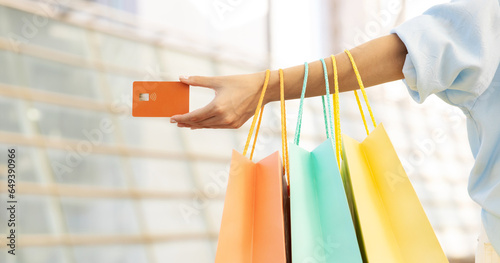 Young european lady shopaholic with bags showing credit card in hand, enjoy shopping and free time in mall, panorama