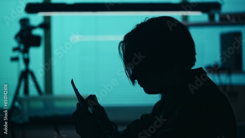 Close up silhouette shot of a suspect, offender, perpetrator or prisoner sitting in the interrogation room. He is studying the evidence in front of him.