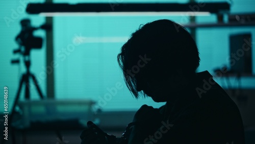 Close up silhouette shot of a suspect, offender, perpetrator or prisoner sitting in the interrogation room. He is looking down with remorse and frustration.