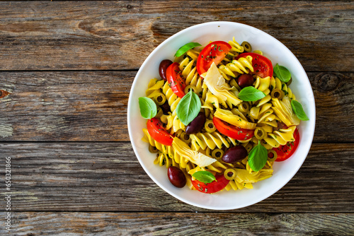 Antipasto pasta salad - fusilli pasta with various vegetables on wooden background
