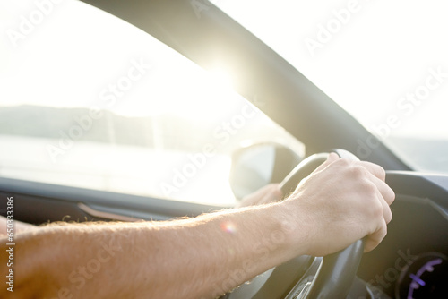 Close-up of a car driver's hands in the rays of the setting or rising sun, sun glare, soft focus
