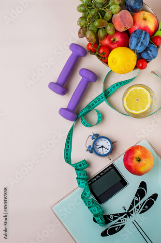 concept of losing weight and physical activity. Scales, dumbbells, tape measure, healthy food, water with lemon, a lot of fresh fruit and a clock, free space for an inscription, top view.