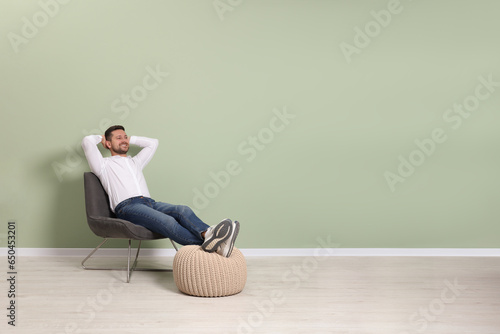 Happy man sitting in armchair near light green wall indoors, space for text