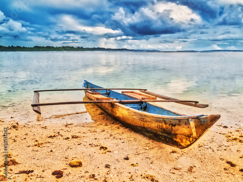 Traditional Indonesian outrigger canoe anchored on the beach of a tropical island