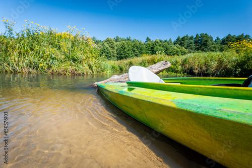 Green kayak on the river. Beautiful sunny day. Sandy yellow river bottom. Blue sky. Wieprz River. Zwierzyniec, Roztocze Region, Poland.