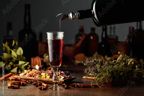 Brown herbal liquor or balm is poured from a vintage bottle into a glass.