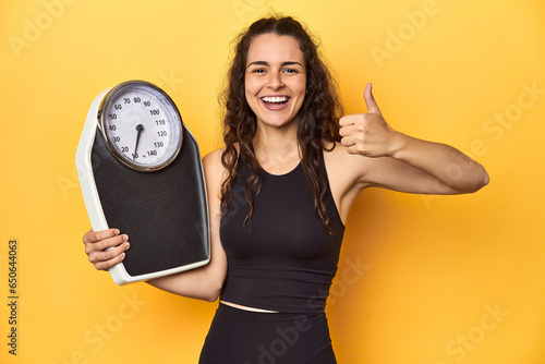 Young Caucasian woman with scale, weight management concept, yellow background.