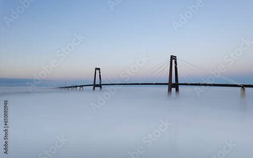 Tranquil, blue-sky scene featuring the Hale Boggs Memorial Bridge shrouded in foggy mist