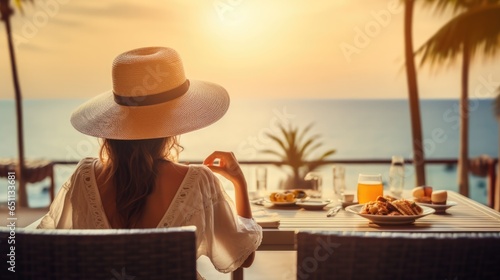 Young woman on summer vacation enjoying breakfast on a luxury hotel resort terrace overlooking the sea.