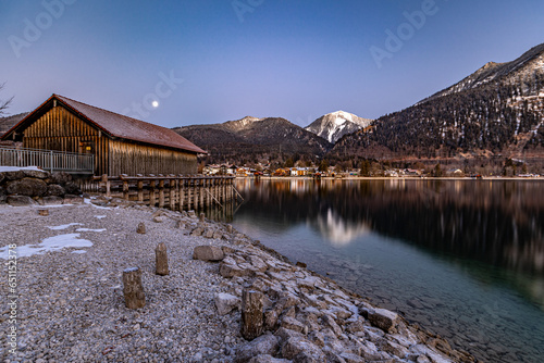 winterliche Morgenstimmung am Walchensee mit Bootshaus und Mond