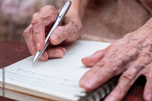close up wrinkled hands for elderly person writing notes on his note book
