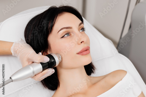 Attractive young woman undergoing a cosmetic procedure in a beauty salon. A woman undergoes fractional RF lifting against a light background. Advertising concept for clean and young facial skin.