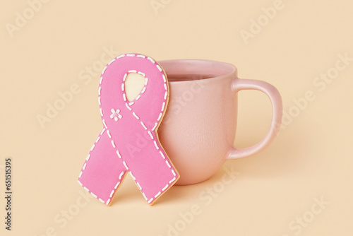 Pink cookie in shape of ribbon and cup of coffee on beige background. Breast cancer awareness concept