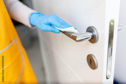 Hand wearing surgical glove while disinfect doorknob with wet wipe