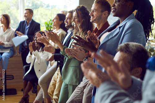 Group of happy joyful business people applaudding to speaker standing in a row in meeting room. Successful coworkers and company employees clapping a colleague on business training or conference.