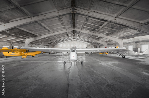 Small airplanes in storage at small aerodrome. Hangar of flying club with light aircraft - propeller driven ones and a glider. 