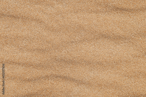Close-up background brown sand wave with rippled dunes. Top view. Space for text. Sand summer texture.
