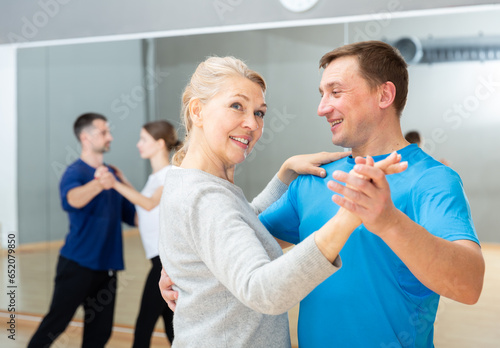 Mature dancing couple enjoying social dance during group class in modern studio