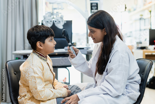 Indian child boy with women eye specialist examining eyesight modern ophthalmology equipment in clinic. Patient kid male checkup iris examines ophthalmological hospital. measure eyeglasses.